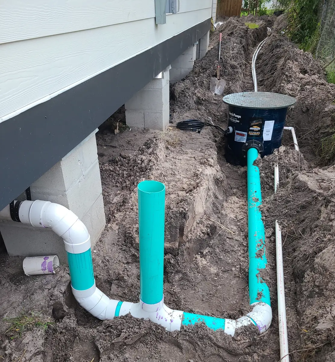 Sanitation main line being tied into a grinder pump in an open trench beside a home
